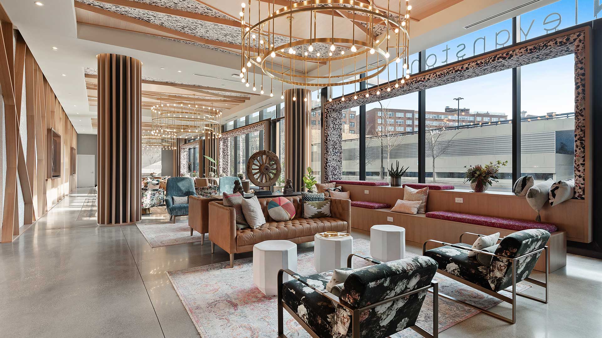 Eva apartment lobby in Evanston with floor-to-ceiling windows, lounge seating, built-in window benches, and statement lighting.