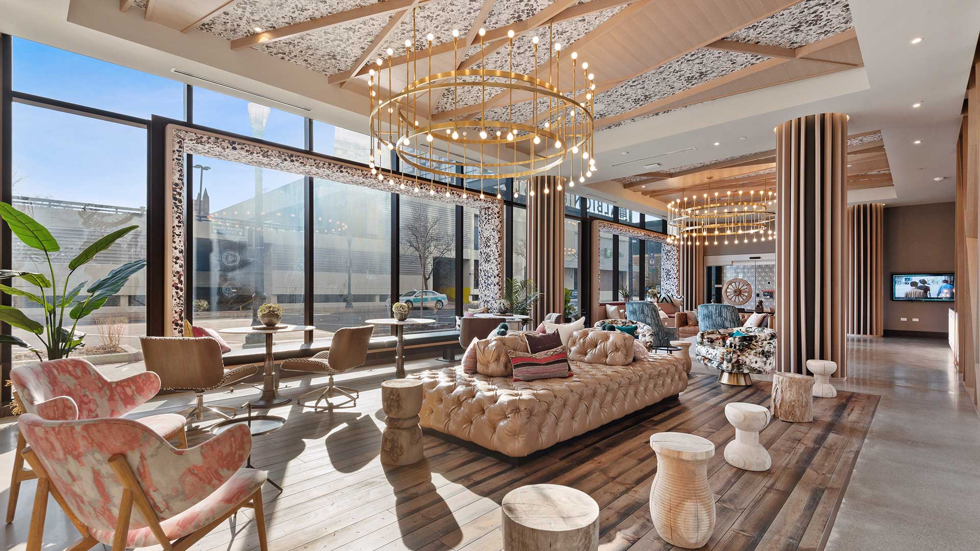 Eva apartment lobby lounge with floor-to-ceiling windows, sofas, lounge chairs, café tables, and statement chandeliers.