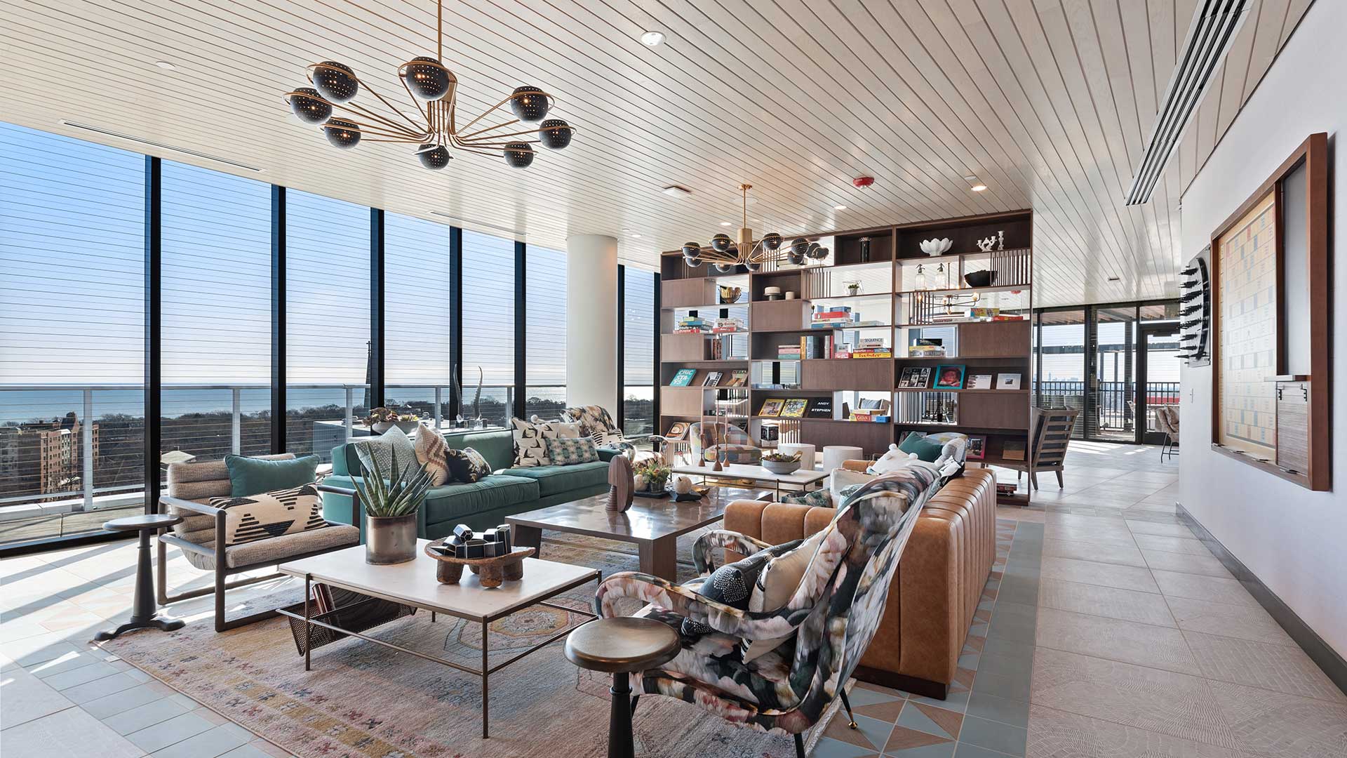 Eva Rooftop Sky Club lounge with sofas, armchairs, library shelving, floor-to-ceiling windows, and views of Lake Michigan.