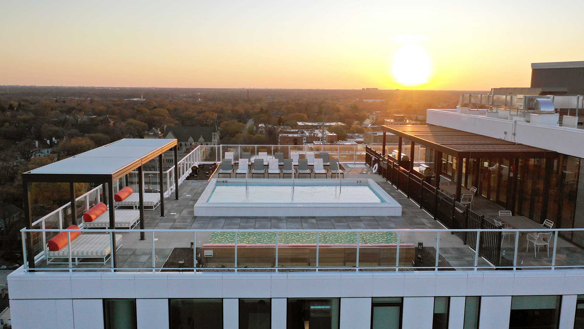 Aerial view of Eva’s rooftop pool and sundeck at sunset with lounge seating and expansive neighborhood views.