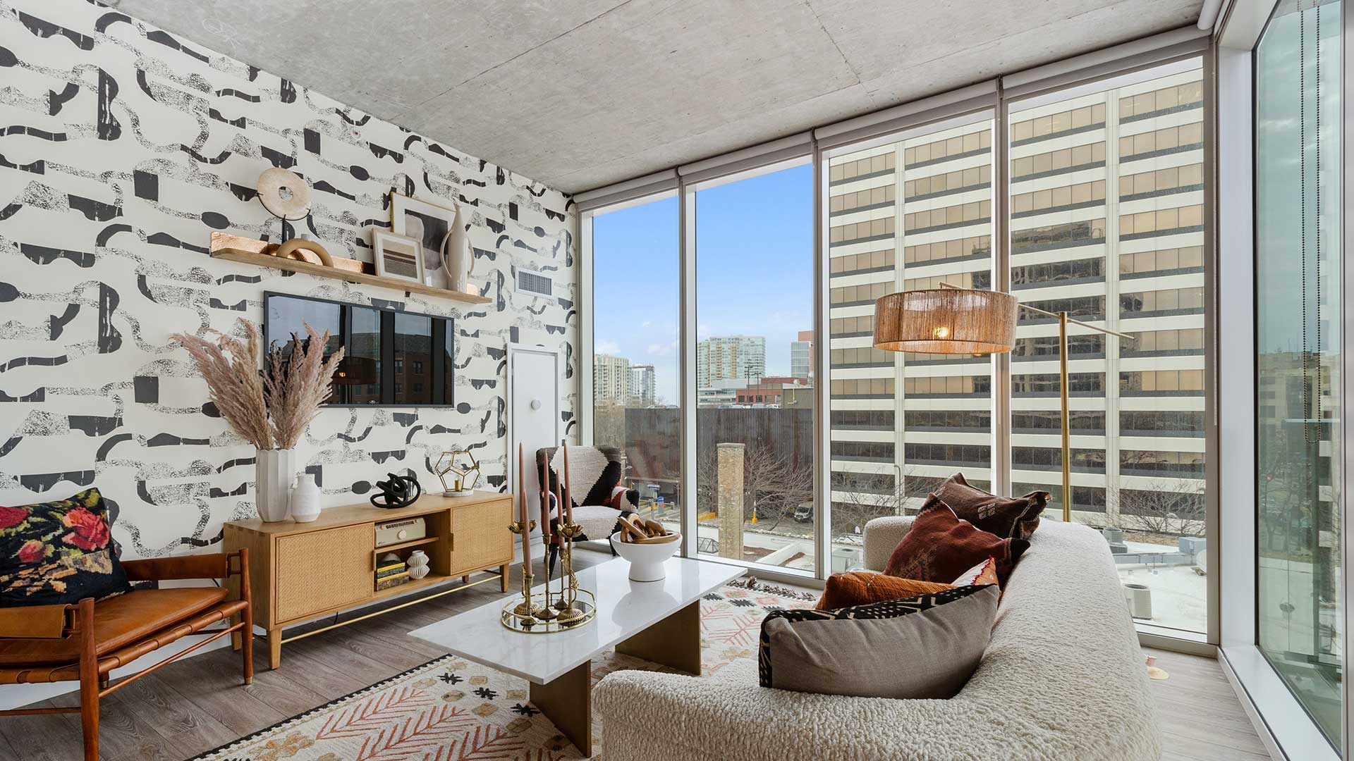Eva apartment living room with floor-to-ceiling windows, modern furnishings, patterned accent wall, and views of downtown Evanston.