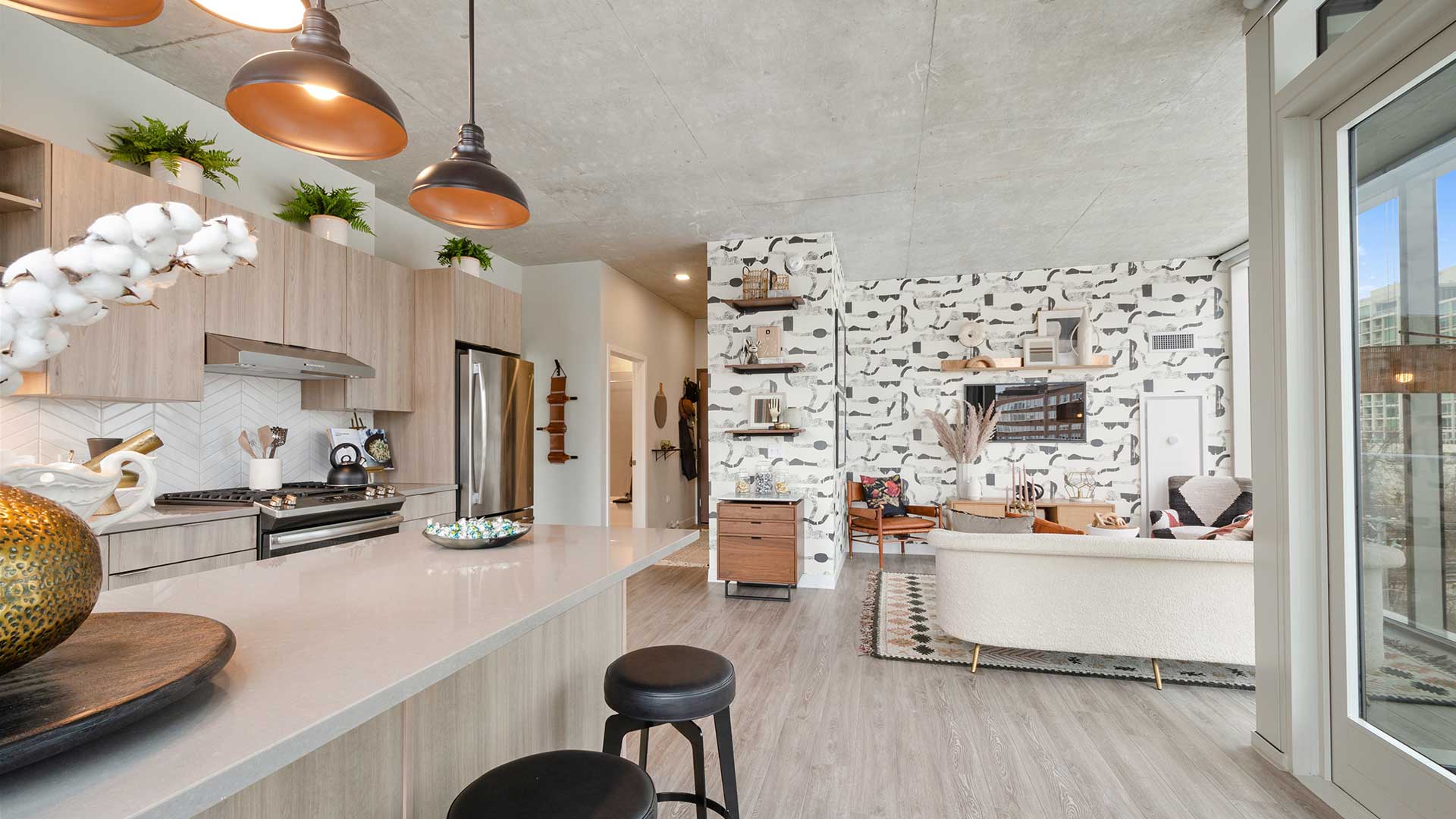 Open-concept apartment interior featuring a kitchen island, stainless steel appliances, modern cabinetry, living area and floor-to-ceiling windows.